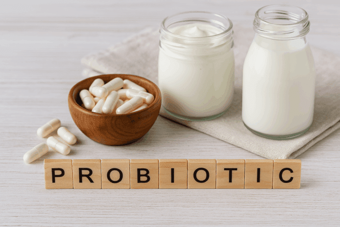 Probiotische Kapseln in Holzschale mit Joghurt und Milchflaschen